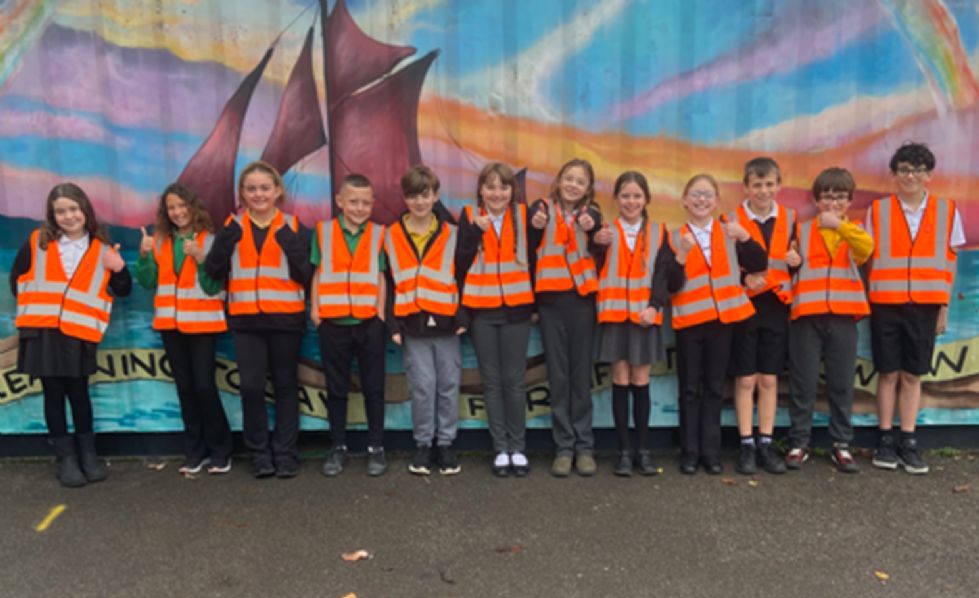 a line-up of children wearing high vis vests in front of a ship mural